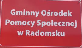 Czerwona tablica z napisem: Gminny Ośrodek Pomocy Społecznej w Radomsku