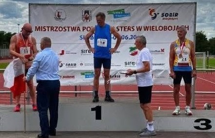 Trzej panowie w sportowych strojach stoją na podium. Pierwszy z prawej Piotr Płoskoński 