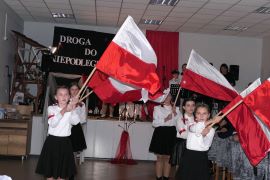 Dziewczynki w galowych strojach trzymają w ręku biało - czerwone flagi