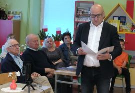 Grupa ludzi: większość siedzi na krzesłach