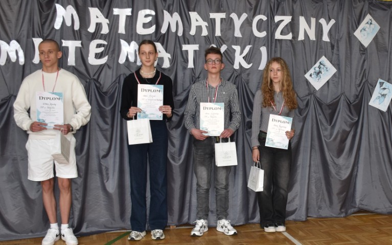 Dwie dziewczyny i dwóch chłopców stoi obok siebie. Wszyscy trzymają w dłoniach dyplomy