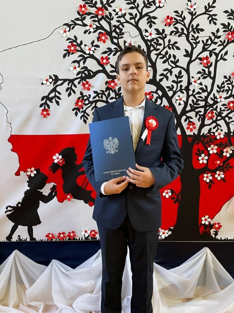 Chłopiec w garniturze. Chłopiec trzyma w ręku dyplom 