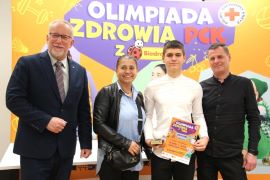 Cztery osoby stoją obok siebie. Chłopiec trzyma w ręku dyplom 