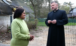 Starsza kobieta w zielonej bluzce stoi obok księdza