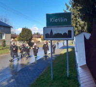 Grupa osób idzie ulicą. Na pierwszym planie widoczna zielona tablica z napisem Kietlin 