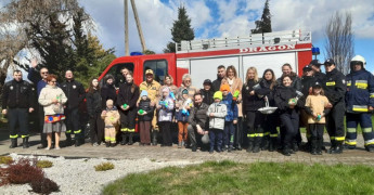 Grupa osób: dorośli i dzieci stoi obok siebie. Osoby stoją na tel wozu strażackiego