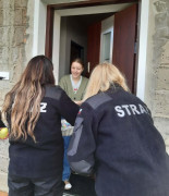 Trzy kobiety. Jedna z nich stroi w drzwiach domu 