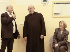 Mężczyzna trzyma mikrofon w ręku. Obok mężczyzny stoi ksiądz