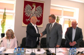 Kobieta i trzech mężczyzn. Kobieta siedzi. Trzej mężczyźni stoją. Dwóch z nich podaje sobie dłonie