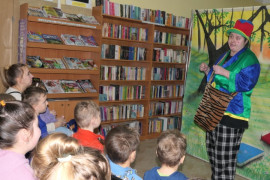 Uczestnicy przedstawienia. Dzieci siedzą na krzesłach. Przed nimi stoi kobieta w kolorowym ubraniu