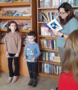 Dziewczynka i dwaj chłopcy słuchają fragmentów książki czytanych przez pisarkę Elżbietę Stępień 