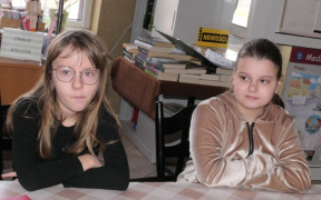 Dwie dziewczynki siedzą obok siebie przy stole 