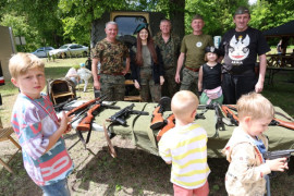 Dorośli i dzieci. Stoisko wystawiennicze, na którym znajdują się repliki broni. Dzieci oglądają repliki m.in. pistoletów 