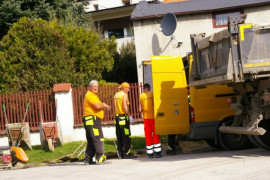 Trzech mężczyzn przy robotach drogowych. Obok stoi samochód ciężarowy