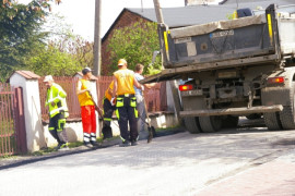 Robotnicy przy budowie drogi. Obok nich stoi samochód ciężarowy