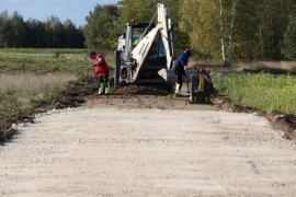 Droga w przebudowie. Widoczna pierwsza warstwa oraz maszyna drogowa 