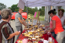 Stoisko wystawiennicze, na którym znajdują się ciasta. Przy stoisku znajdują się cztery osoby