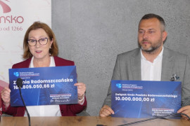 Kobieta i mężczyzna siedzący za stołem prezydialnym. Osoby prezentują niebieskie tabliczki, na których widnieją kwoty pieniędzy, jakie w ramach rządowego programu POLSKI ŁAD trafią na Ziemię Radomszczańską 