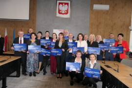 Grupa osób trzymających w rękach niebieskie tabliczki, na których widnieją kwoty pieniędzy, jakie w ramach rządowego programu POLSKI ŁAD trafią do miast, powiatów i gmin 