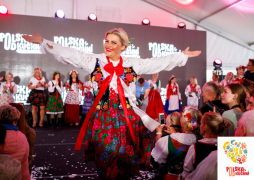 Kobieta w ludowych stroju. Otacza ją grupa osób 