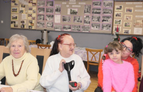 Trzy kobiety siedzące przy stole. Na kolanach jednej z nich siedzi mała dziewczynka 