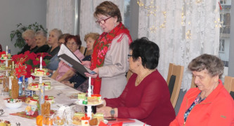Grupa kobiet siedzi przy stole. Jedna z nich stoi i przemawia 