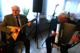 Dwóch panów siedzących na krzesłach i grających na instrumentach 