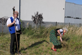 Kobieta ścinająca sierpem zboże, obok której stoi mężczyzna z cepem 