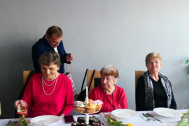 Trzy kobiety siedzą przy stole. Mężczyzna wręcza im słodki podarunek