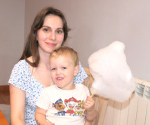 Kobieta trzyma na kolanach chłopca. Chłopiec ma w ręku watę cukrową 