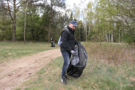 Mężczyzna ubrany na sportowo trzyma w ręku worek na śmieci. Mężczyzna uczestniczy w akcji sprzątania brzegów rzeki Warty