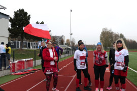 Grupa osób w sportowych strojach. Jedna z nich trzyma w ręku biało-czerwoną flagę 
