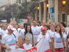 Grupa osób, w białych koszulkach. Trzy z nich trzymają flagę Polski 