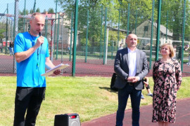 Kobieta i dwóch mężczyzn na murawie boiska. Mężczyzna w błękitnej bluzce trzyma mikrofon w ręku 
