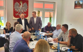 Grupa osób podczas posiedzenia. Dwóch mężczyzn stoi obok siebie