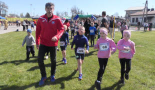 Mężczyzna w dresie oraz grupa dzieci w sportowych strojach podczas biegu 