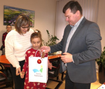 Mężczyzna wręcza dziewczynce prezent. Obok dziewczynki stoi kobieta