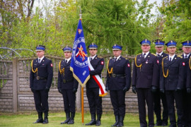 Mężczyźni w mundurach w szeregu. Jeden z nich trzyma sztandar