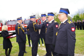 Pięciu mężczyzn w mundurach strażackich. Dwóch z nich wręcza odznaczenia. Kobieta trzyma w dłoniach tacę, na której znajdują się odznaczenia