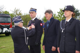 Dwóch mężczyzn i kobieta w mundurach strażackich. Jeden w cywilnym ubraniu. Mężczyzna w mundurze wręcza odznaczenia