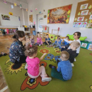 Grupka przedszkolaków siedzi w kręgu na dywanie, 2 kobiety prowadzą warsztaty