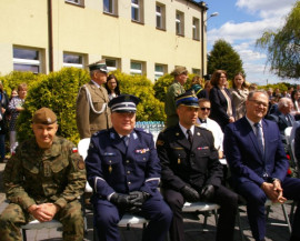 Czterech mężczyzn siedzi na krzesłach. Trzech jest w mundurach, jeden w garniturze