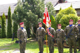 Grupa żołnierzy w mundurach moro i czerwonych beretach na głowach. Jeden z nich trzyma sztandar