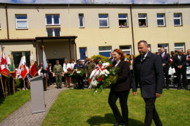 Mężczyzna i kobieta w cywilnych ubraniach idą złożyć wiązankę kwiatów. Kwiaty niesie kobieta