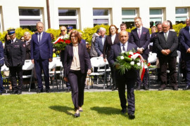 Kobieta i mężczyzna w marszu. Mężczyzna trzyma wiązankę kwiatów. W oddali widać grupę ludzi