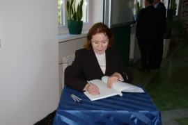 Kobieta siedząc przy stoliku dokonuje wpisu do pamiątkowej ksiegi