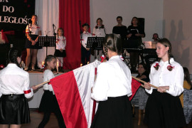 Dziewczynki w galowych strojach. Każda z nich trzyma w ręku biało-czerwoną flagę 