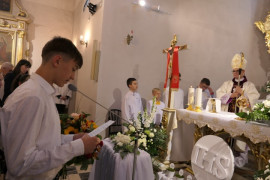 Chłopiec w białej bluzce stojąc przed ołtarzem dziękuje biskupowi za dar bierzmowania