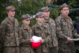 Grupa harcerzy. Jeden z nich trzyma w ręku złożoną flagę Polski