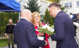 Mężczyzna i kobieta (wójt Gminy Radomsko i dyrektor PSP w Kietlinie) wręczają kwiaty mężczyźnie (wiceministrowi Cieciórze)